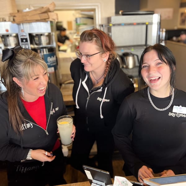 Three Sassy Onion staff members, Tiffany, Tori, and another, laughing together behind the counter.