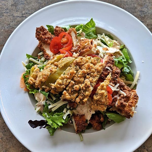 A Sassy Onion salad with fried chicken, fried pickles, lettuce, tomatoes, and cheese.