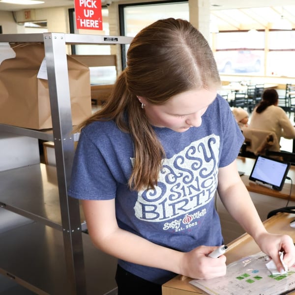 A Sassy Onion employee in a blue shirt marks a checklist at a pickup counter.
