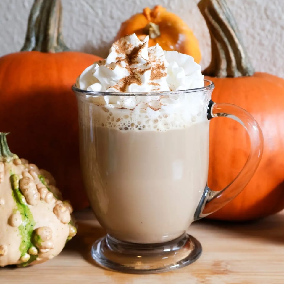 Pumpkin spice latte with whipped cream and cinnamon, surrounded by pumpkins and gourds.