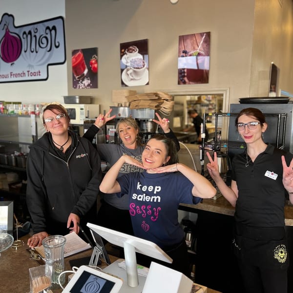 Four Sassy Onion staff members smiling and posing behind the counter, with restaurant decor in the background.