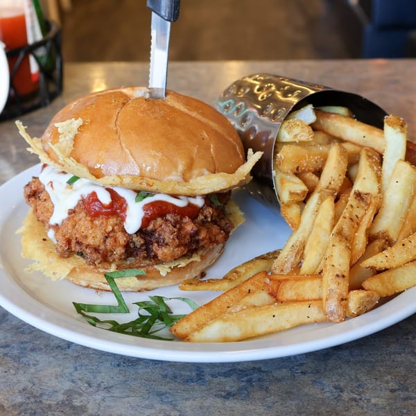 Sassy Onion's crispy chicken sandwich with fries, topped with sauce and a knife.