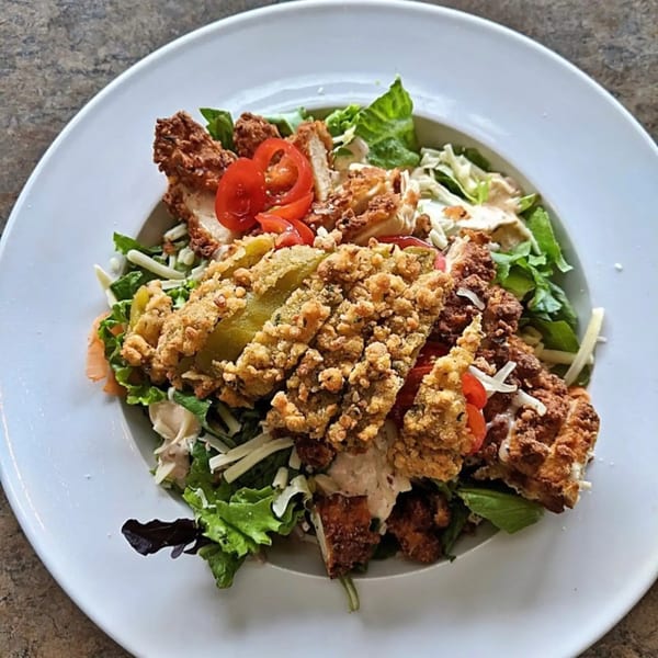 A Sassy Onion fried chicken and pickle salad with lettuce, tomatoes, and shredded cheese.