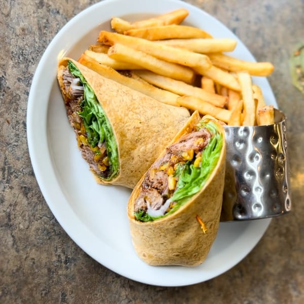 Two halves of a Sassy Onion wrap with meat, lettuce, and onions, served with french fries.