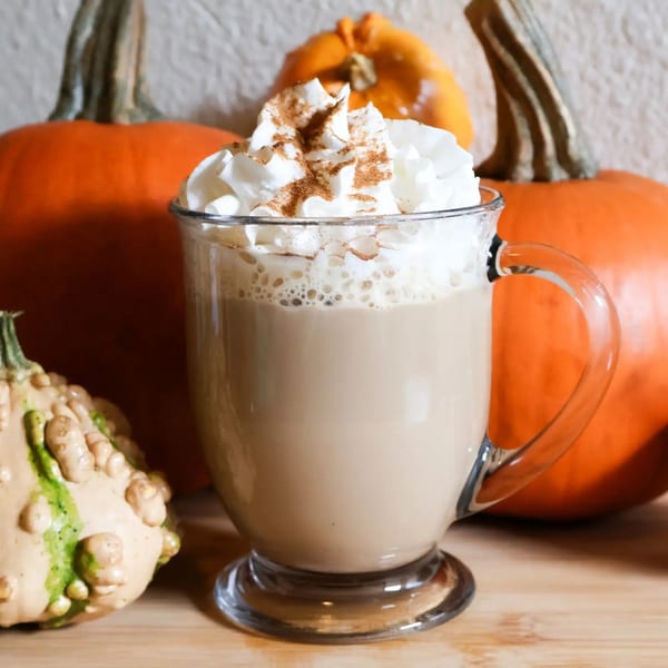 A pumpkin spice latte with whipped cream and cinnamon, surrounded by pumpkins and gourds.