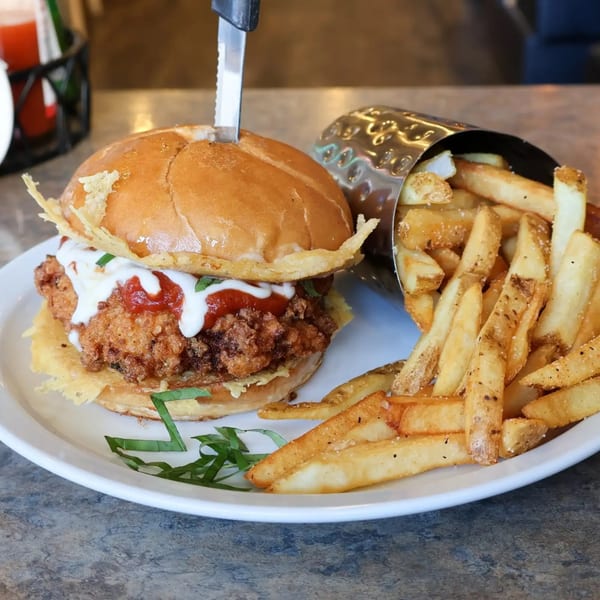 Sassy Onion's fried chicken sandwich with ketchup, white sauce, and a side of french fries.